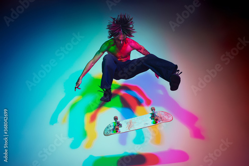 Fototapeta Naklejka Na Ścianę i Meble -  Skateboarder doing a trick isolated on studio background in colorful neon light. Young man shirtless riding and skateboarding in motion. Concept of leisure activity, sport, extreme, hobby and motion.