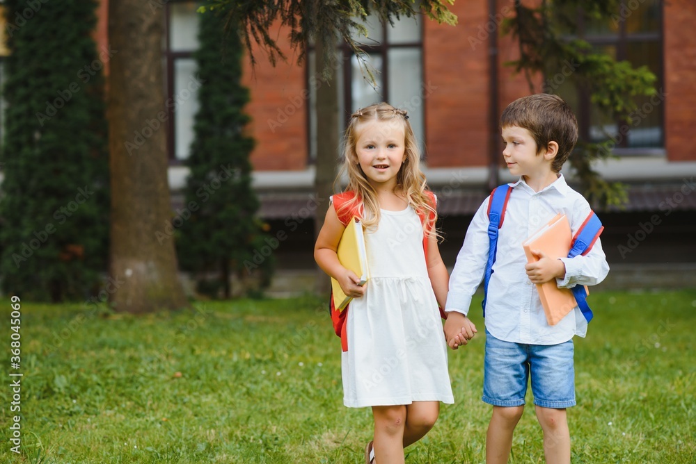 Happy children - boy and girl with books and backpacks on the first school day. Excited to be back to school after vacation. Full length outdoor portrait. Happy children - boy and girl with books and backpacks on the first school day. Excited to be back to school after vacation. Full length outdoor portrait.