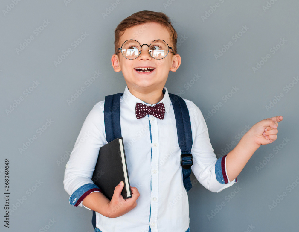 Cheerful, mischievous boy holds a book in his hands, standing at the blackboard. an excited child on a grey background directs its attention to the free space. Back to school. Cheerful, mischievous boy holds a book in his hands, standing at the blackboard. an excited child on a grey background directs its attention to the free space. Back to school.