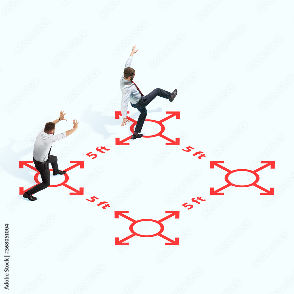 Studio shot of people demonstrating social distancing with arrows indicating the separation. Office workers during coronavirus outbreak with new rules for safety and healthcare. High angle view