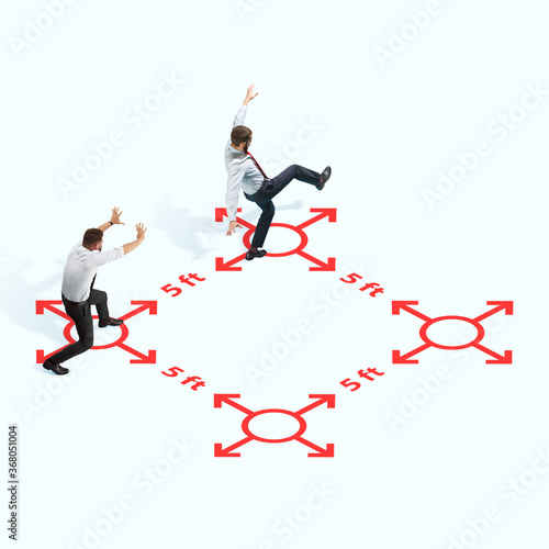 Studio shot of people demonstrating social distancing with arrows indicating the separation. Office workers during coronavirus outbreak with new rules for safety and healthcare. High angle view