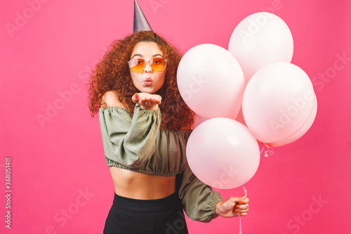 Happy holiday! Happy young curly smiling woman with balloons isolated over pink background. Valentines day or womans day.