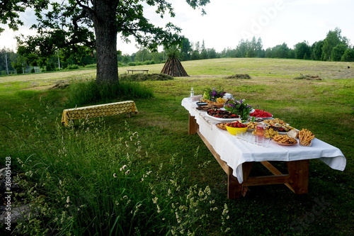 Wooden table under oaks with many traditional Latvian food. Old Latvian culture tradition LIGO. Midsummer night celebrating in Latvia. 