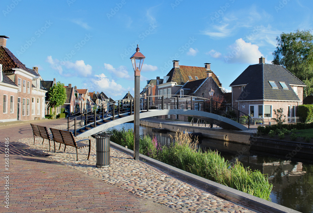 The quaint town of Kollum in Friesland in the Netherlands on a sunny summer's evening. View of the Trekvaart waterway, waterfront houses and the pedestrian bridge.