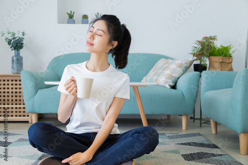 Young asia woman with ponytail in white t-shirt holding a cup of coffee or tea relaxing at home in the morning.