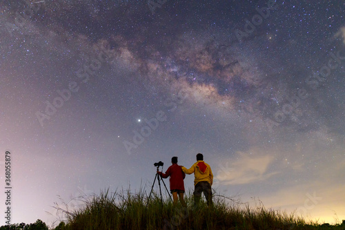 Night time long exposure landscape photography.the milky way,A couple standing in a high place looking up in wonder to the Milky Way galaxy, photo composite.
