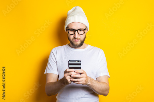 Serious focused young man with a beard holding a phone on a yellow background