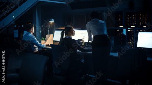 Late at Night In Modern Office: Diverse Team of Successful Businessmen and Businesswomen Work on Desktop Computers, Having Discussion, Finding Problem Solutions, Finishing Project 