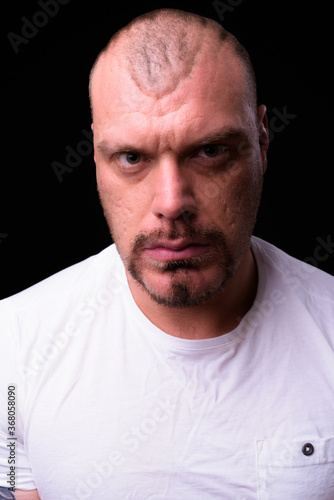 Face of muscular bald bearded man against black background