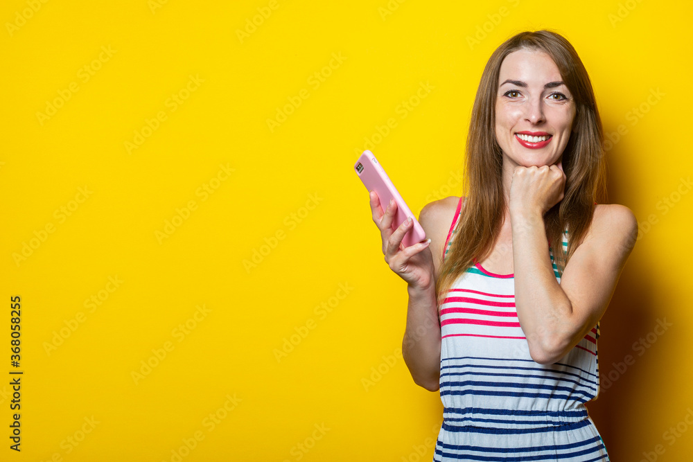 Smiling young girl holding a phone and holding her hand under her chin on a yellow background Smiling young girl holding a phone and holding her hand under her chin on a yellow background