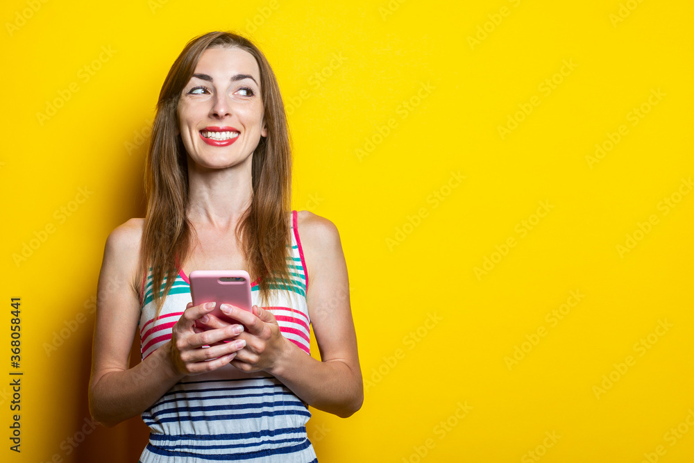 Cute young woman with phone smiling looks aside on a yellow background. Banner. Cute young woman with phone smiling looks aside on a yellow background. Banner.