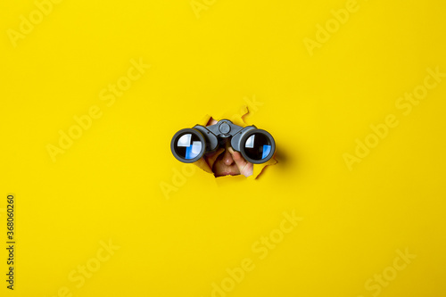 Fototapeta Female hand holds black binoculars on a yellow background