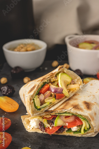 Vegan tortilla wrap stuffed with hummus and fresh vegetables placed on dark background. Ready to eat.
