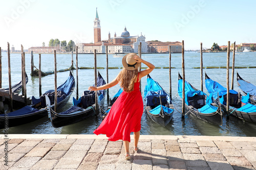 Holidays in Venice. Back view of beautiful girl in red dress enjoying view of Venice Lagoon with the island of San Giorgio Maggiore and gondolas moored. © zigres