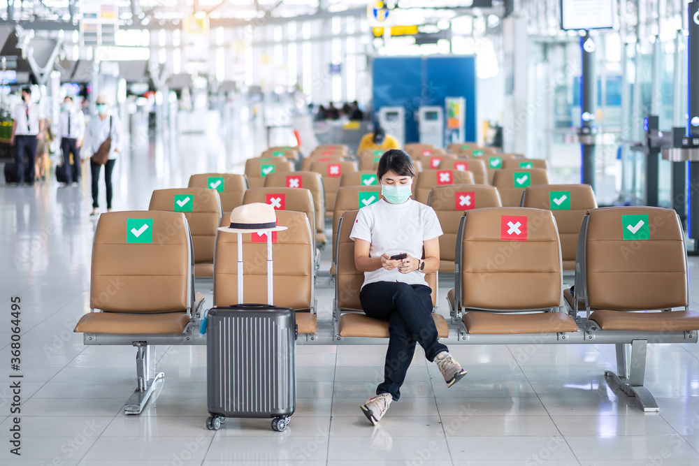 Young female wearing face mask and using mobile smartphone in airport, protection Coronavirus disease (Covid-19) infection, Asian woman traveler sitting on chair. New Normal and social distancing Young female wearing face mask and using mobile smartphone in airport, protection Coronavirus disease (Covid-19) infection, Asian woman traveler sitting on chair. New Normal and social distancing