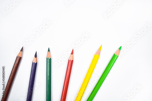 Seven different colored wood pencil crayons placed on a white background