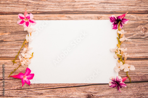 Pink azalea flowers with white asystasia gangetica flowers and blank paper sheet on a wooden background.spring border pink and white blossom  top view  Blank template for banner. flat lay.