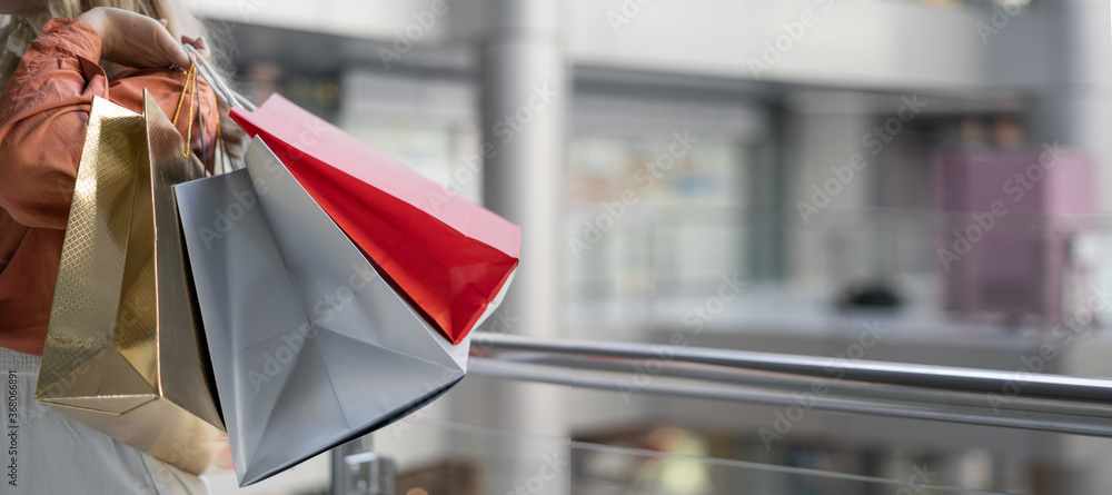 Close-up of bright paper bags in female hands. Beautiful blonde makes purchases in the mall.