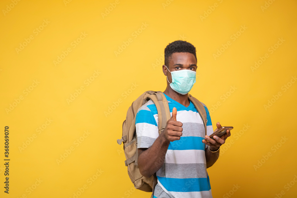 a young black man carrying a backpack and wearing a face mask using his mobile phone, gives a thumbs up a young black man carrying a backpack and wearing a face mask using his mobile phone, gives a thumbs up