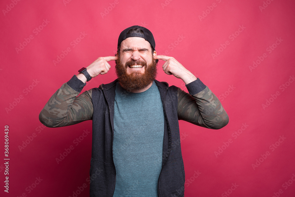 Stressed man with eyes closed is covering his ears over pink background. Stressed man with eyes closed is covering his ears over pink background.