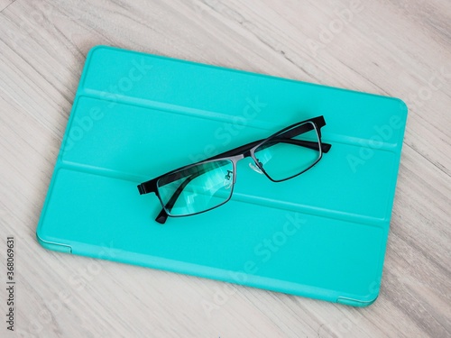Valokuva Closeup shot of reading glasses with light blue leather folio case for tablet