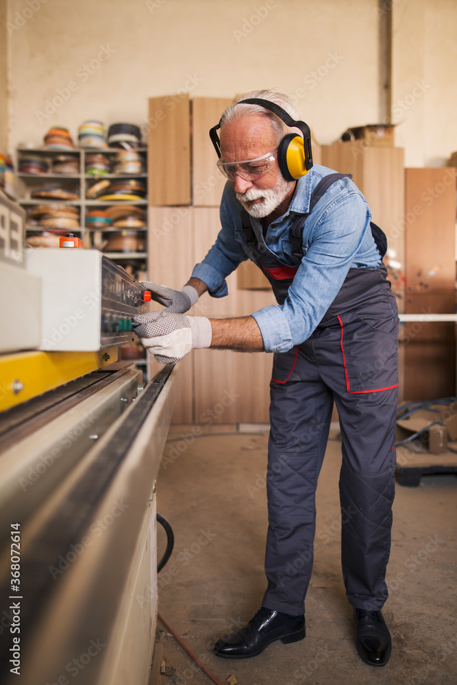 Elderly craftsman adjusting buttons on a woodworking machine Elderly craftsman adjusting buttons on a woodworking machine