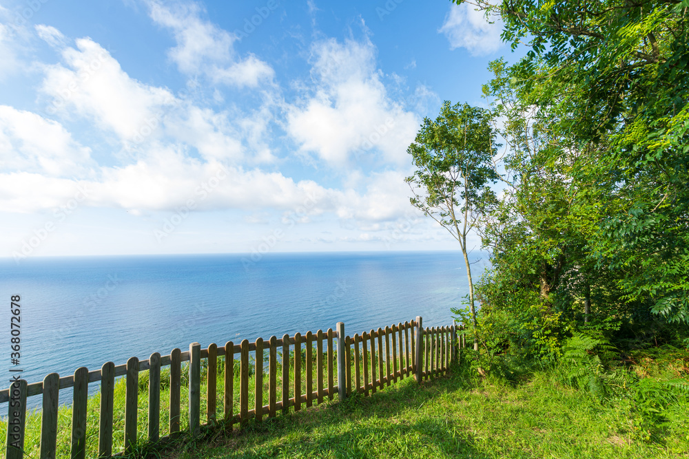 Landscape with fence, trees and meadow overlooking the sea, a sunny afternoon in Elorriaga, Basque Country, Spain, horizontal
