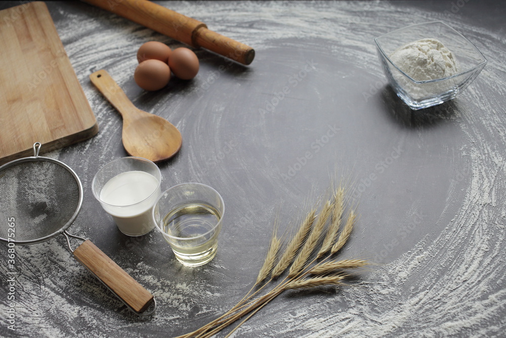 Egg, flour, olive oil, milk, wheat ears, kitchen tool on gray table background. Egg, flour, olive oil, milk, wheat ears, kitchen tool on gray table background.