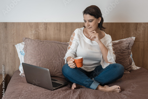 young woman doing home office, holding a cup, with her laptop computer.