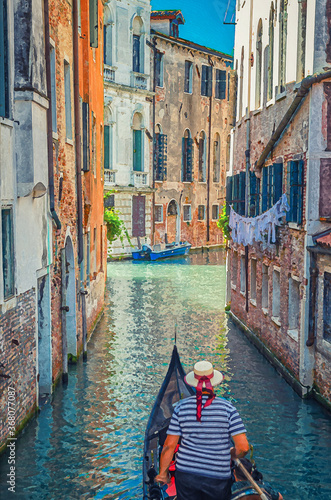 Watercolor drawing of Gondola sailing narrow canal in Venice between old buildings with brick walls. Gondolier dressed traditional clothes and boater straw hat with red ribbon.