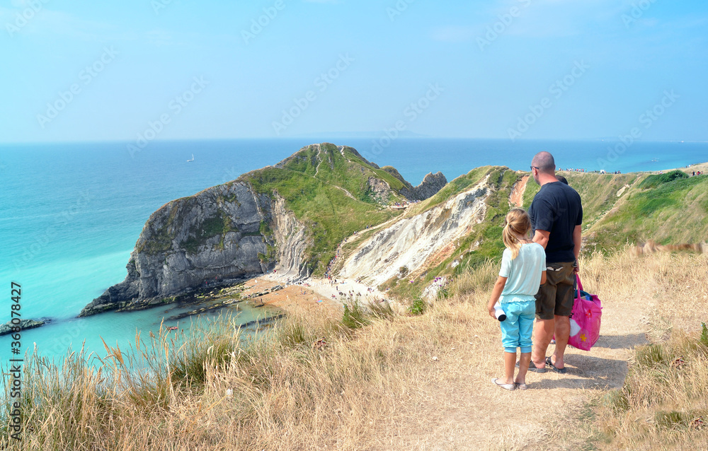 Durdle Door, England - July 21 2013: Family visiting magic landmark in Dorset, Jurassic Coast. Father and daughter climb the hill after the sunbath. Holiday in South of UK during Summer.