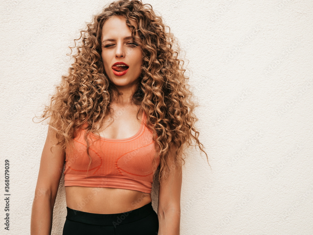 Beautiful smiling model with afro curls hairstyle dressed in summer hipster clothes.Sexy carefree girl posing in the street near white wall.Funny and positive woman having fun.Shows tongue Beautiful smiling model with afro curls hairstyle dressed in summer hipster clothes.Sexy carefree girl posing in the street near white wall.Funny and positive woman having fun.Shows tongue