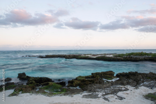 Nightfall at the bay tropical beach. Long exposure shot of the turquoise color sea, blurred ocean waves and rocks in Tulum, Mexico.  © Gonzalo