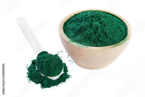  Drewniana miska wypełniona zielonymi algami w proszku, obok łyżka ze spiruliną