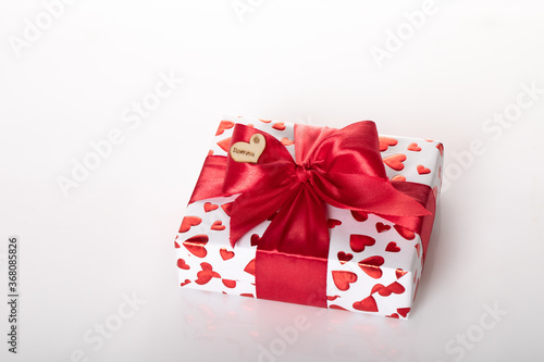 Gift box wrapped in white paper with red heart texture. And wrapped in a pink ribbon.