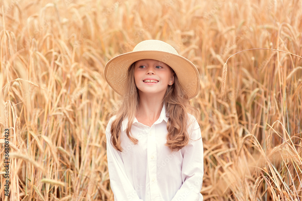 Obraz premium Happy child in wheat field. Beautiful girl with white hair in a straw hat with ripe wheat