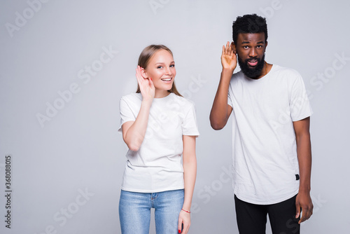 Young mixed couple listen something isolated on white background