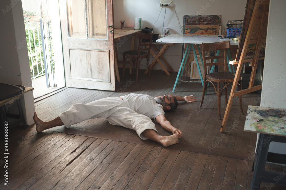 Man in white clothes stretching his legs lying on the wooden floor in a studio Man in white clothes stretching his legs lying on the wooden floor in a studio
