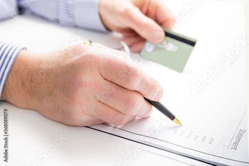 a man holds his credit card and checks his statement with a pen on a white background