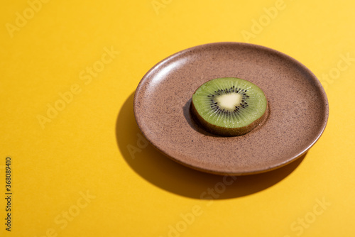 Kiwi slice grows from brown dish over yellow. Concept dieting. Measuring food quantities. Planning healthy meals and desserts