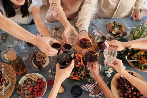 High angle view of people sitting at festive table having dinner and toasting with glasses of red wine