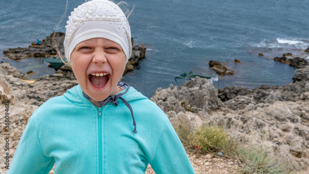 Girl at sea screams, rejoices in a jacket around the mountain, a girl in a hat on the beach Girl at sea screams, rejoices in a jacket around the mountain, a girl in a hat on the beach