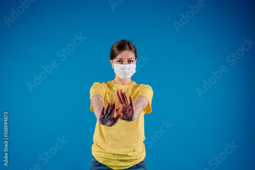 Woman in a protective medical mask on her face on blue background, shows with hands stop sign