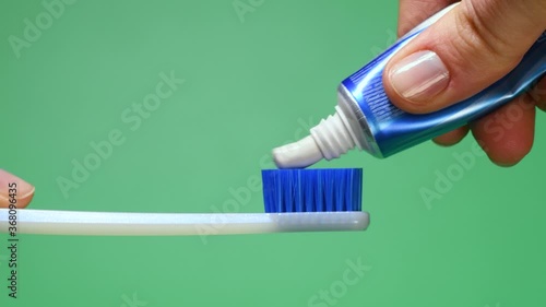 Female hand squeezing tooth paste on blue toothbrush. Green background.