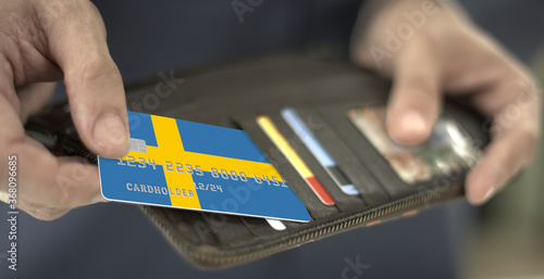 Man pulls plastic card with flag of Sweden out of his wallet, fictional card number