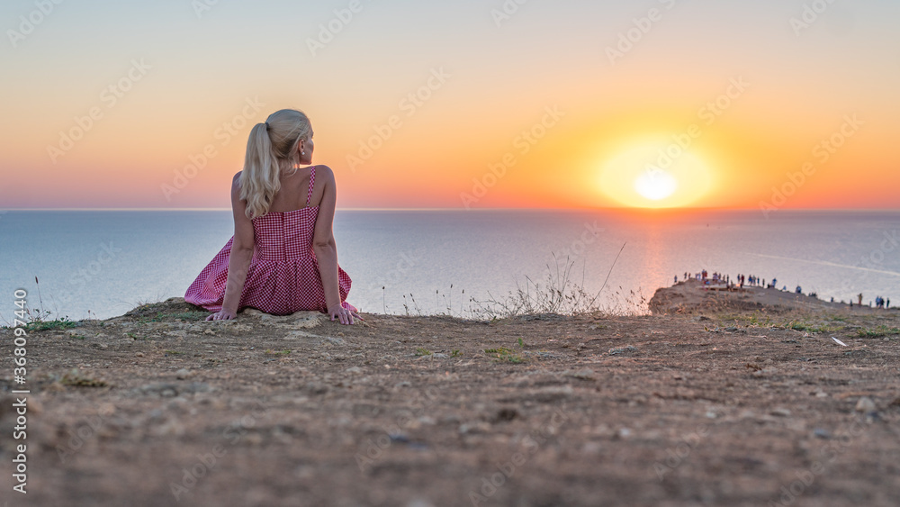 A young girl looks at the sunset stands to the sun face in the summer evening A young girl looks at the sunset stands to the sun face in the summer evening