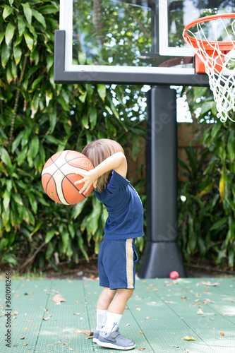 Small Boy child prepares to shoot basketball into basket outdoors