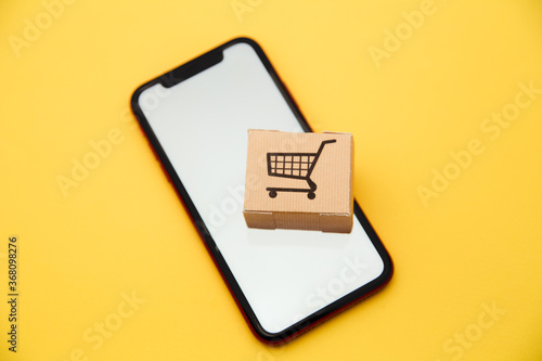 Online shopping and ecommerce via internet concept : box and smartphone on yellow background.