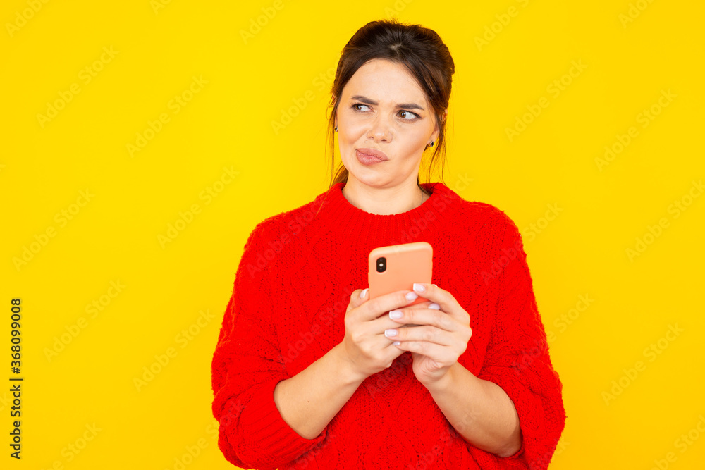 Thinking young woman with phone isolated over the yellow backgroung Thinking young woman with phone isolated over the yellow backgroung