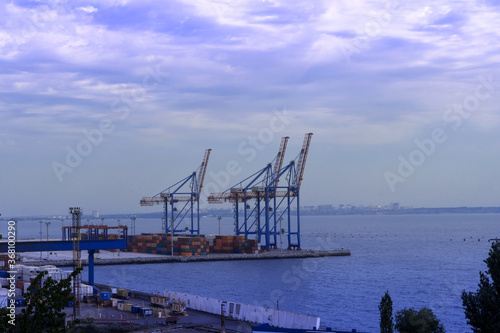 Seaport area, large cranes and stacked shipping containers against the backdrop of the sea